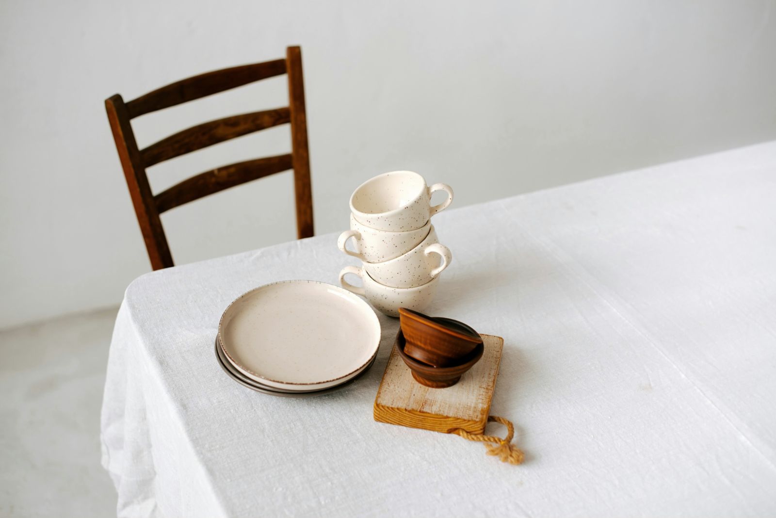 A table laid with ceramic plates and cups beside a wooden chair