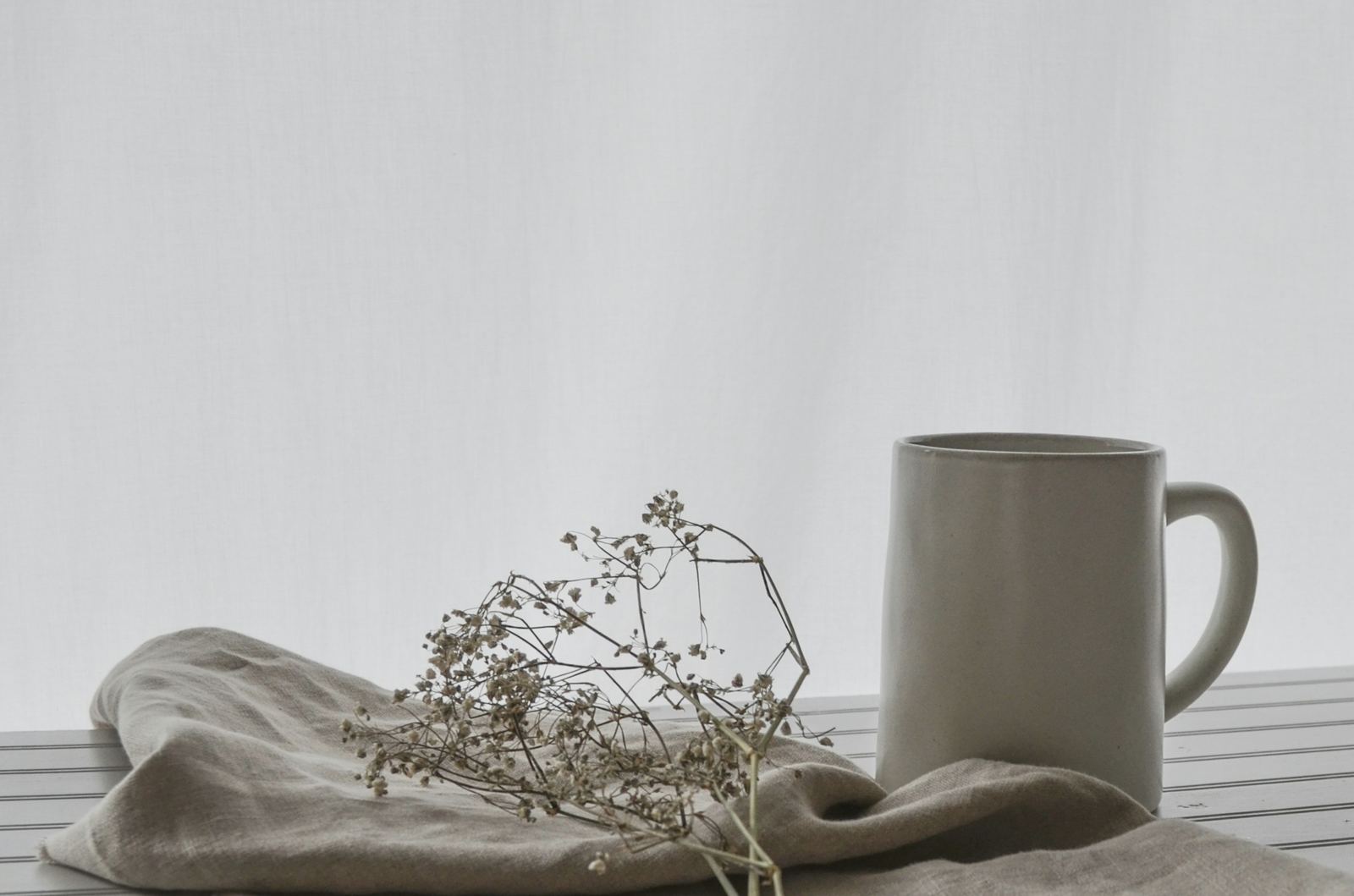 A ceramic mug beside folded linen and dried flowers